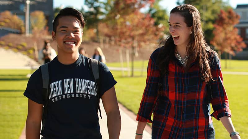 A female student walking and laughing with a male student on the SNHU campus green space