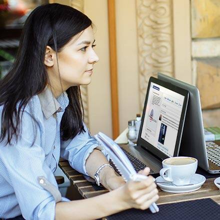Woman holding up a notebook while her laptop is open next to her