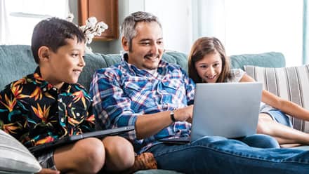 SNHU student sitting on the couch on a laptop with two children