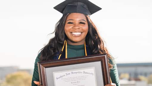 Tanzania Fair, a 2020 graduate of Southern New Hampshire University, wearing her cap and gown and holding her framed SNHU diploma.