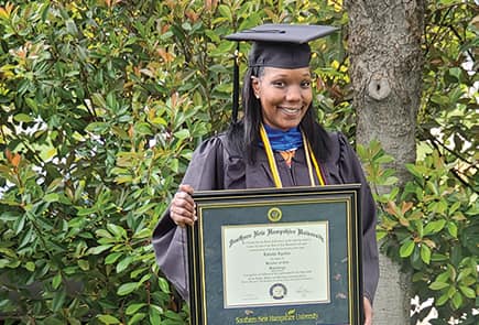 SNHU Graduate Latisha Aguilar holding up a framed degree in front of the woods