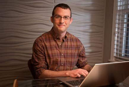 Male online student sitting at a desk on his laptop while smiling at the camera