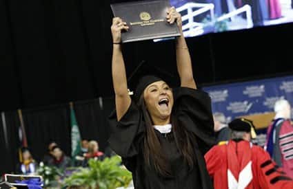 Female student celebrating as she holds up her diploma at a past SNHU graduation ceremony.