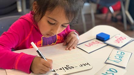 A young girl writing using a marker in a notebook at SNHU's Center for New Americans.