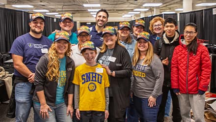 A group of SNHU staff standing around a young boy who is wearing a yellow SNHU T-shirt.