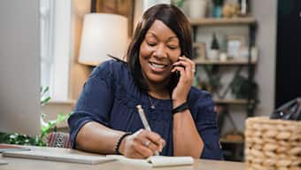 SNHU student speaking on the phone and taking notes in a home office