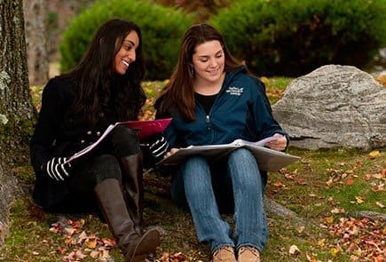 Two women studying outside sitting on the grass