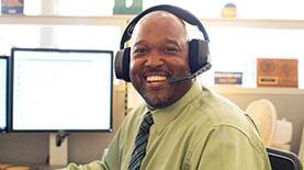 SNHU Employee sitting at his desk smiling with a headset on.