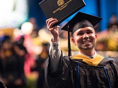 Man holding up his diploma and smiling at the Commencement event