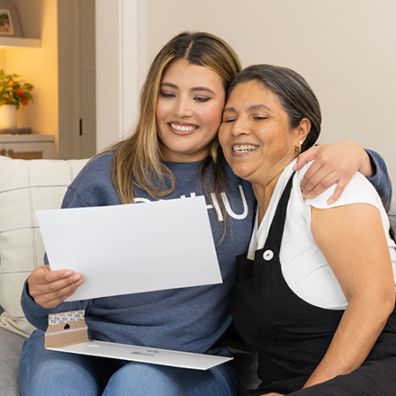 Juliana Zambrano, a 2025 SNHU graduate with a bachelor's degree in business administration sitting on a couch with family looking at her diploma.