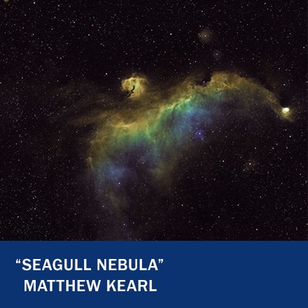 A green, yellow and blue nebula in the shape of a bird in space with the text "Seagull Nebula" Matthew Kearl